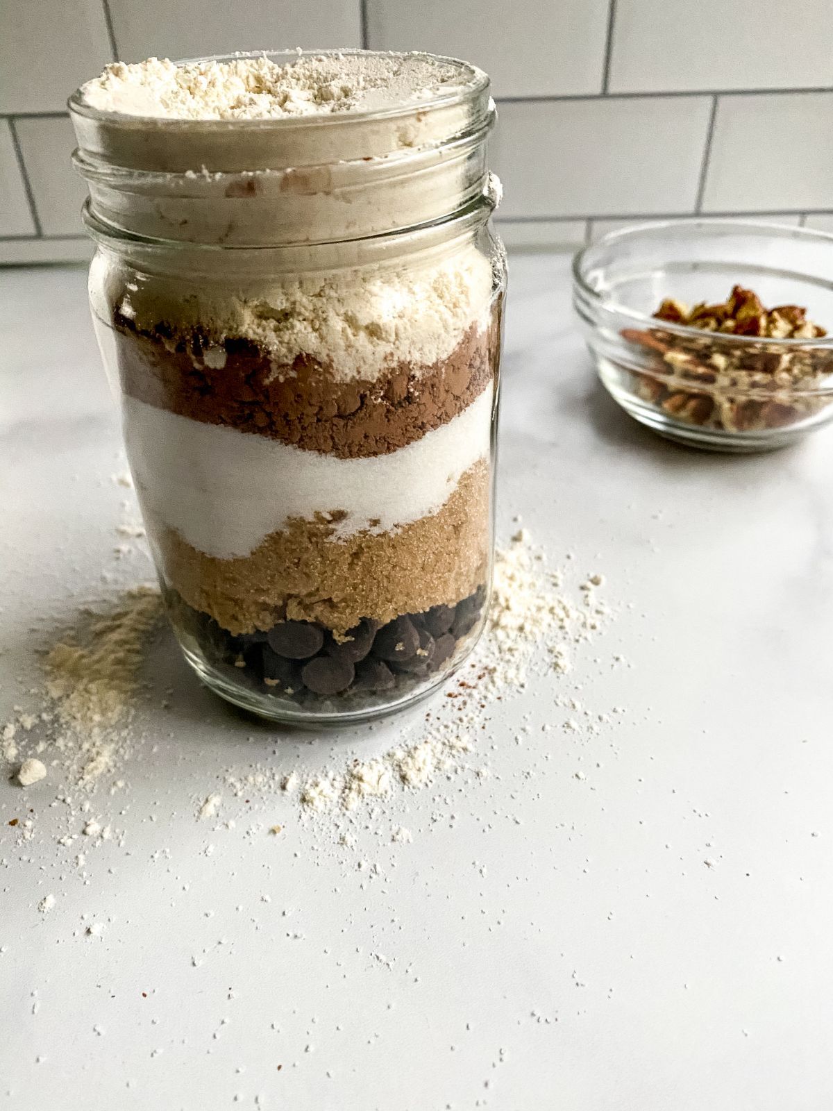 Brownie Mix in a jar freshly assembled next to nuts in a glass bowl.
