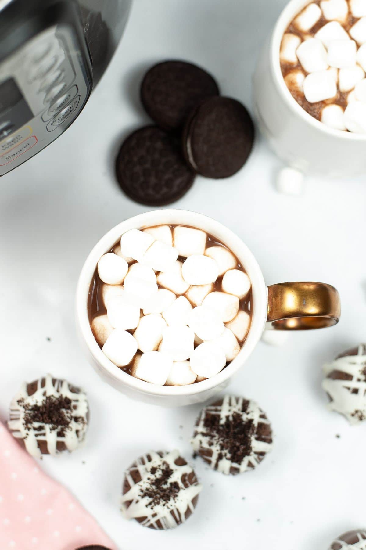 A cup of hot cocoa with marshmallows on top and the Cookies and Cream Hot Cocoa Bombs surrounding the cup.