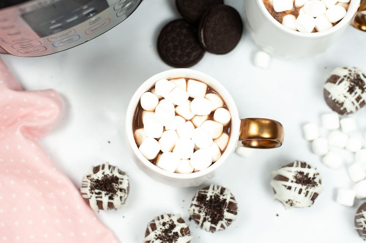A cup of hot cocoa with marshmallow toppings and the Cookies and Cream Hot Cocoa Bombs surrounding the cup.