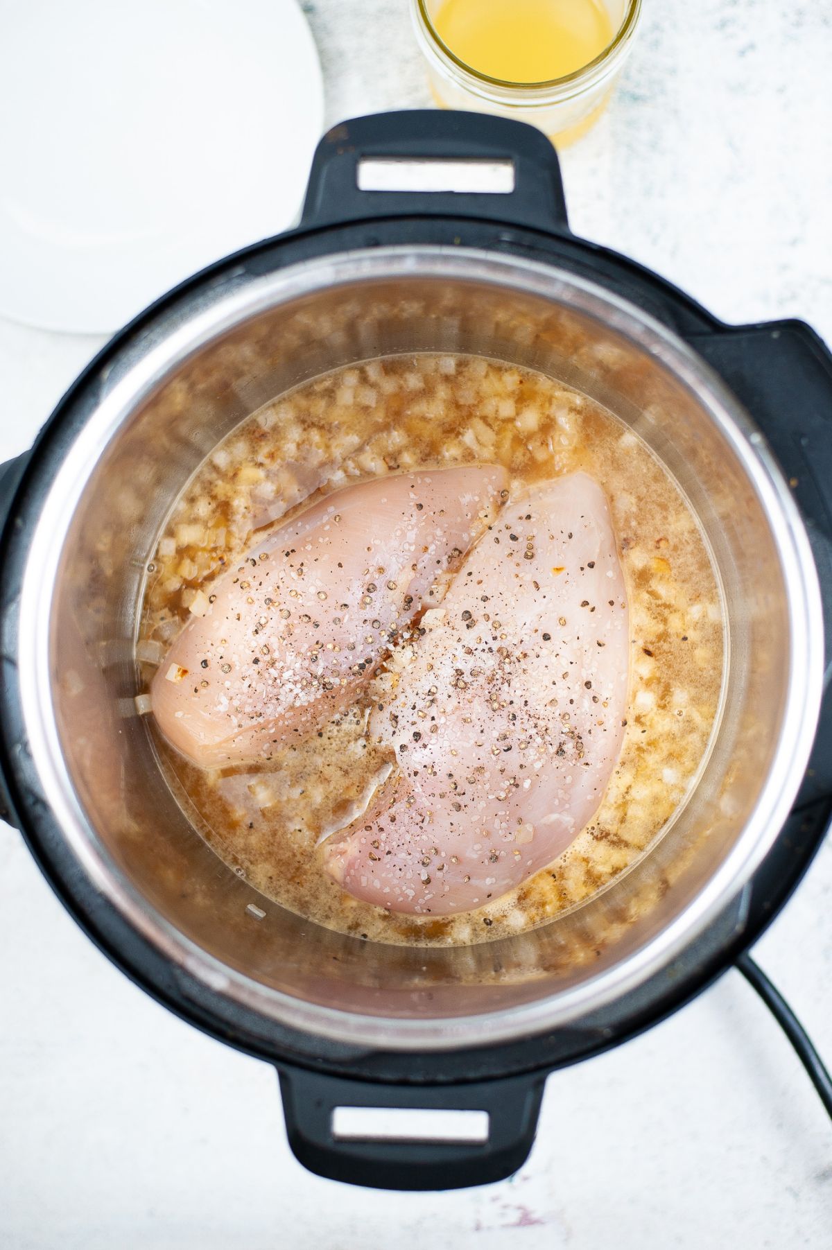 Chicken breasts, broth, onion, salt and pepper being cooked in the instant pot.