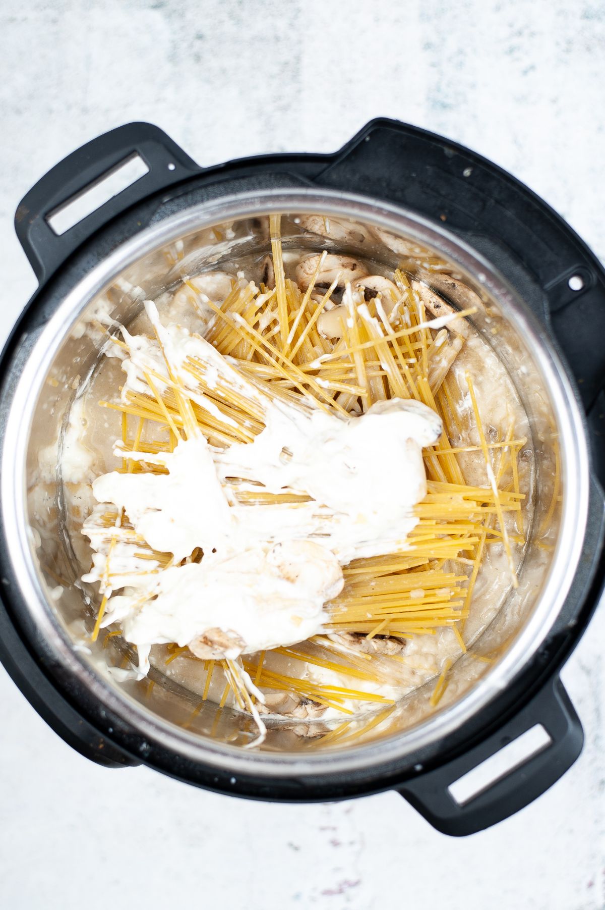 Shredded chicken in the instant pot topped with the other ingredients: pasta, mushroom, sour cream, and broth.