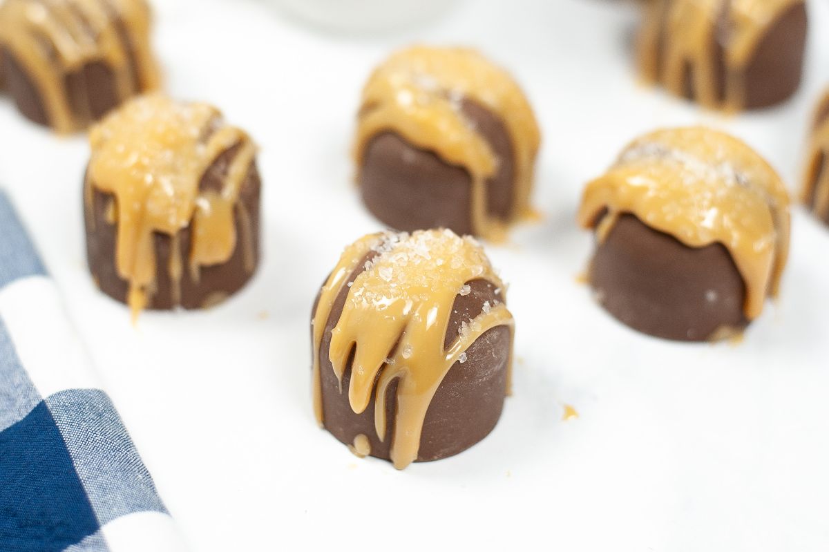 A horizontal angled shot of a batch of Instant Pot Salted Caramel Hot Cocoa Bombs, highlighting the salt and caramel toppings of the caramel bomb in front while the other caramel bombs are blurred in the background.