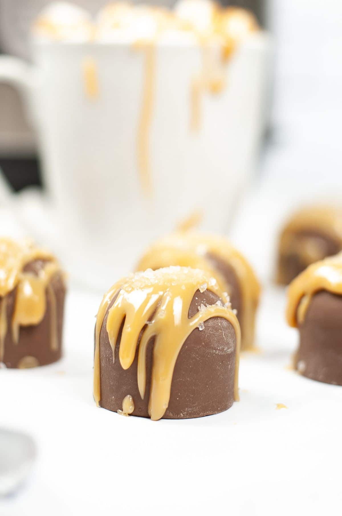 A vertical image of a batch of Instant Pot Salted Caramel Hot Cocoa Bombs, highlighting the salt and caramel toppings of the caramel bomb in front.