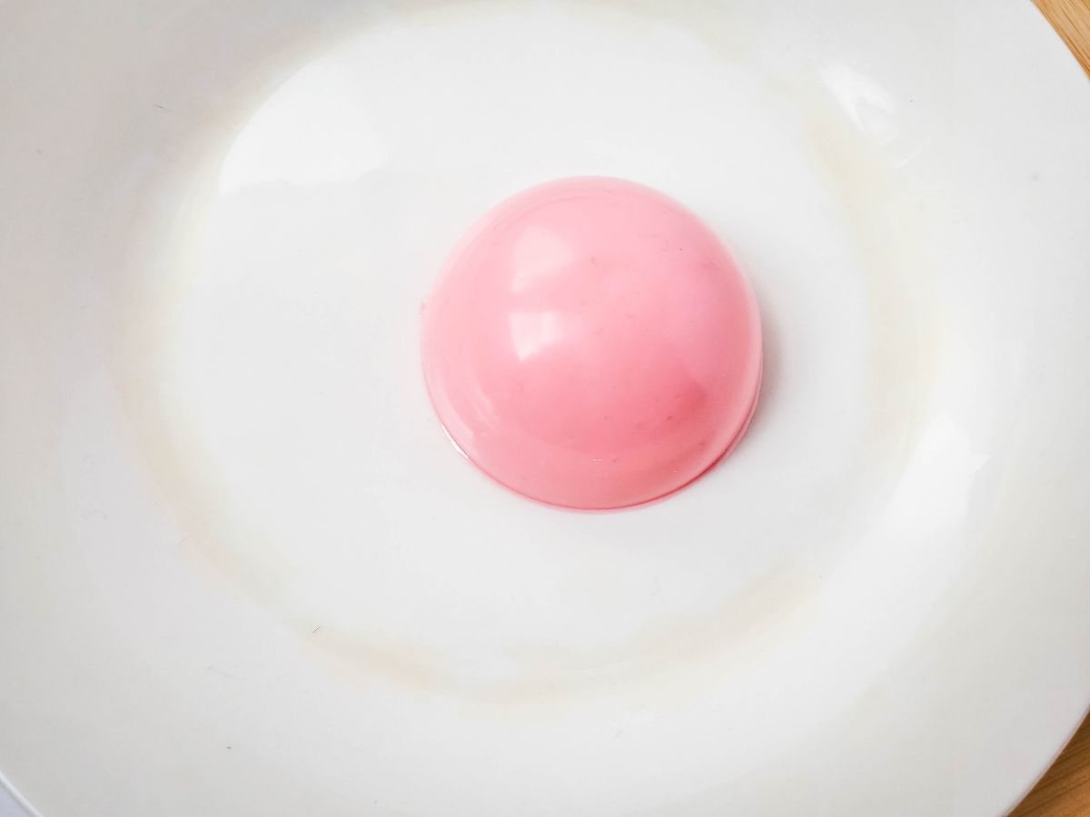 Candy-coated half-sphere placed upside down on a white plate.