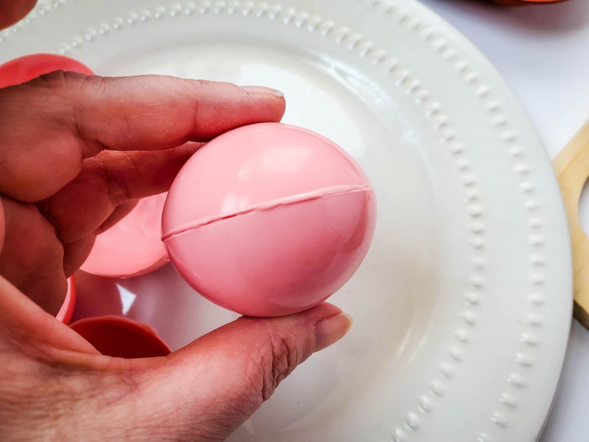 a hand holding two half-sphere candies secured together by melted candy forming a sealed sphere.