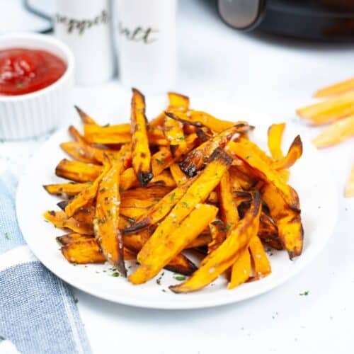 Air fryer sweet potato fries on a plate with ketchup.