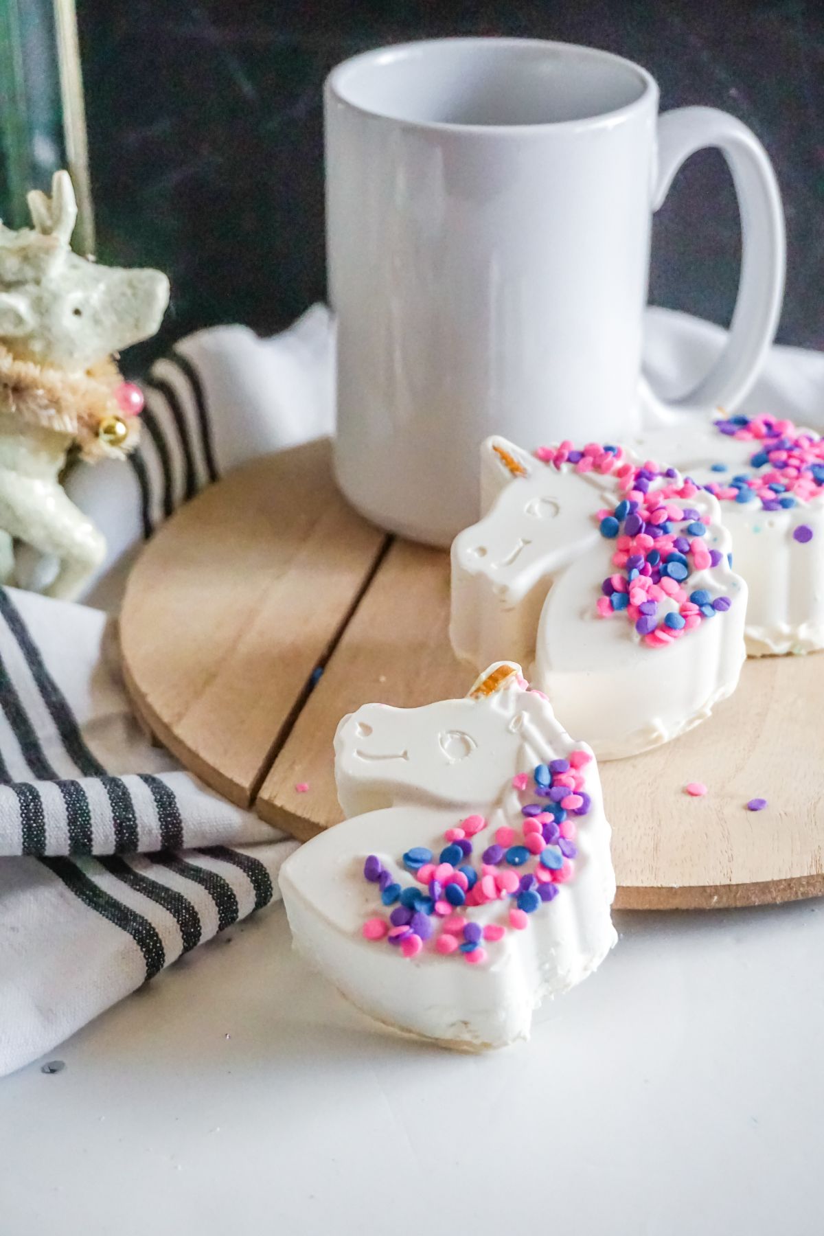 Unicorn Hot Cocoa Bombs on a wooden coaster with a white mug above them.