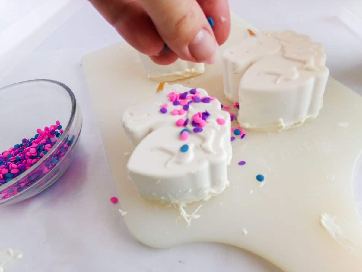 Unicorn Hot Cocoa Bombs being decorated with pink and purple sprinkles.