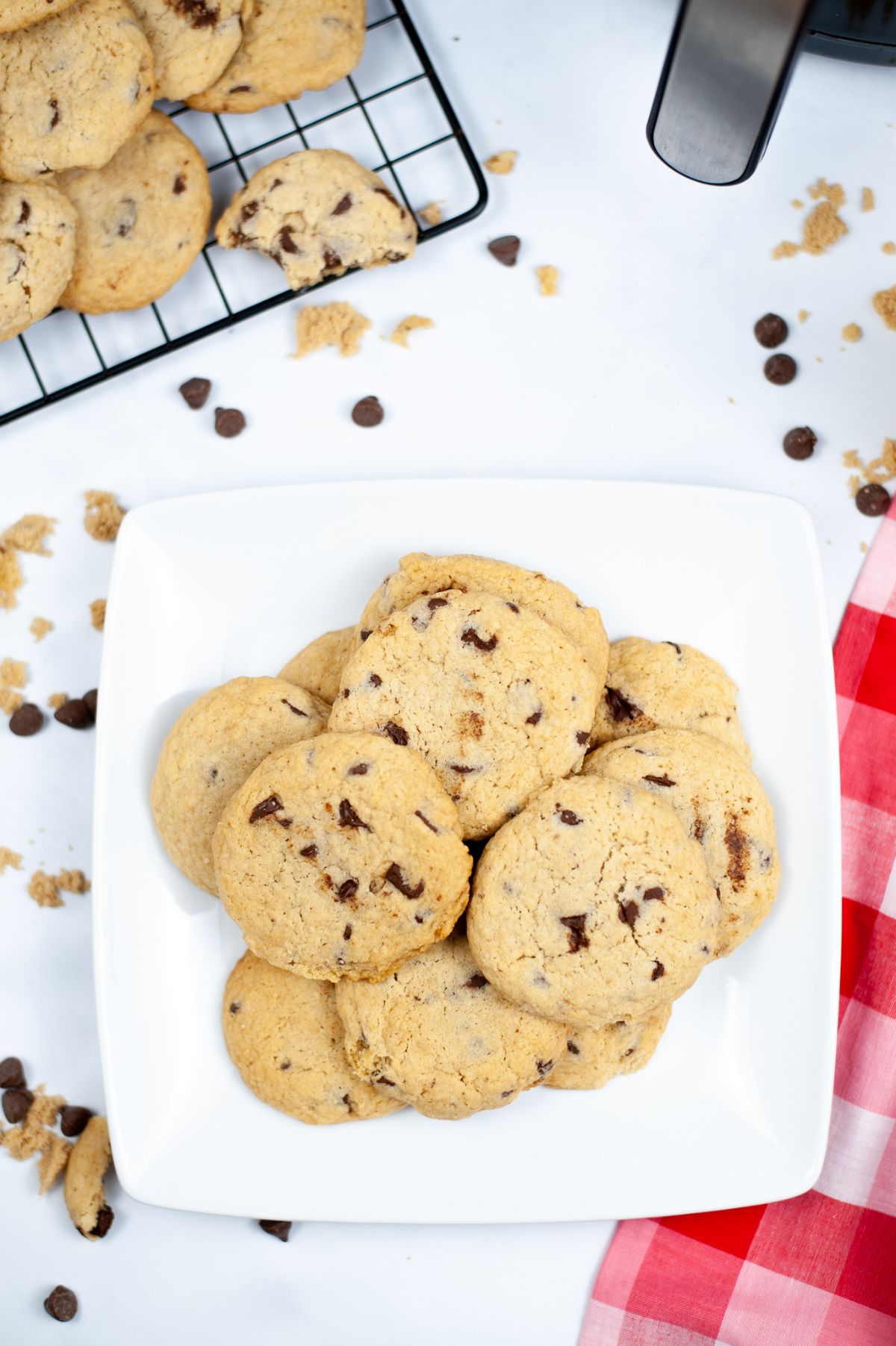 An overhead vertical shot of Air Fryer Chocolate Chip Cookies on a white serving plate with the rest of the cookies on the upper left corner of the image placed on a cooling rack.