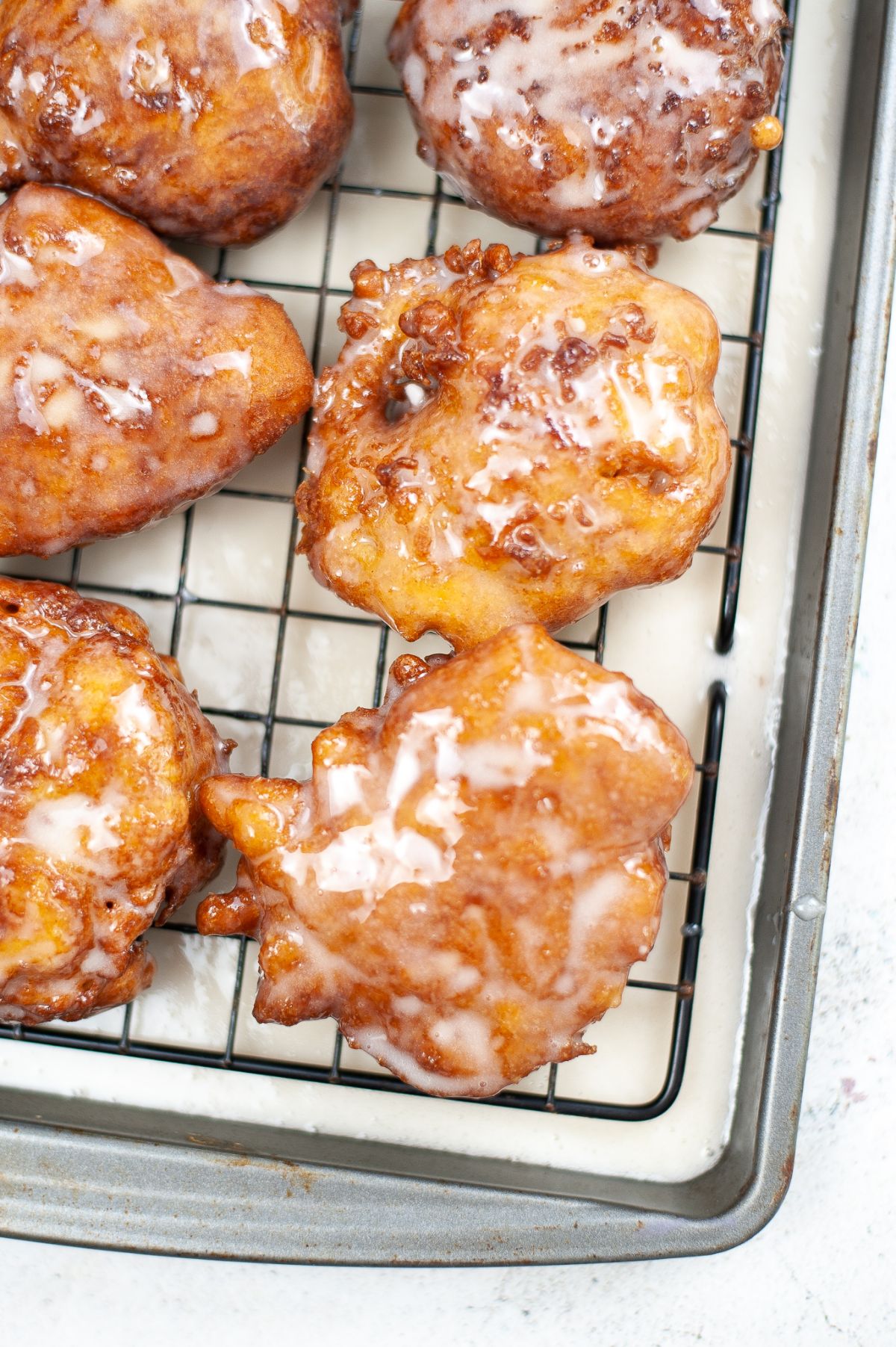 close up of Cooked apple fritters freshly glazed on a cooling rack.