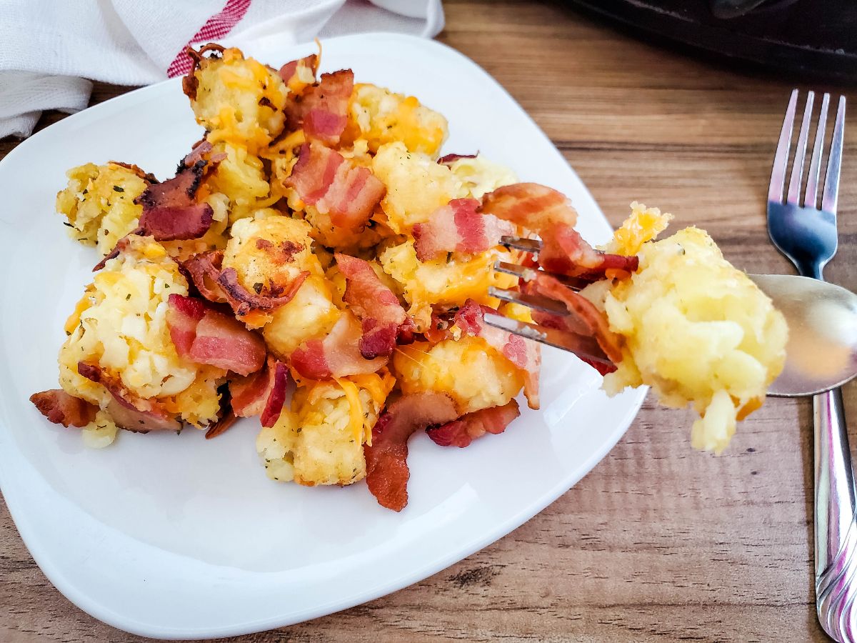 A portion of Cheesy Bacon Ranch Tots on a fork and the rest of the serving on a white plate.