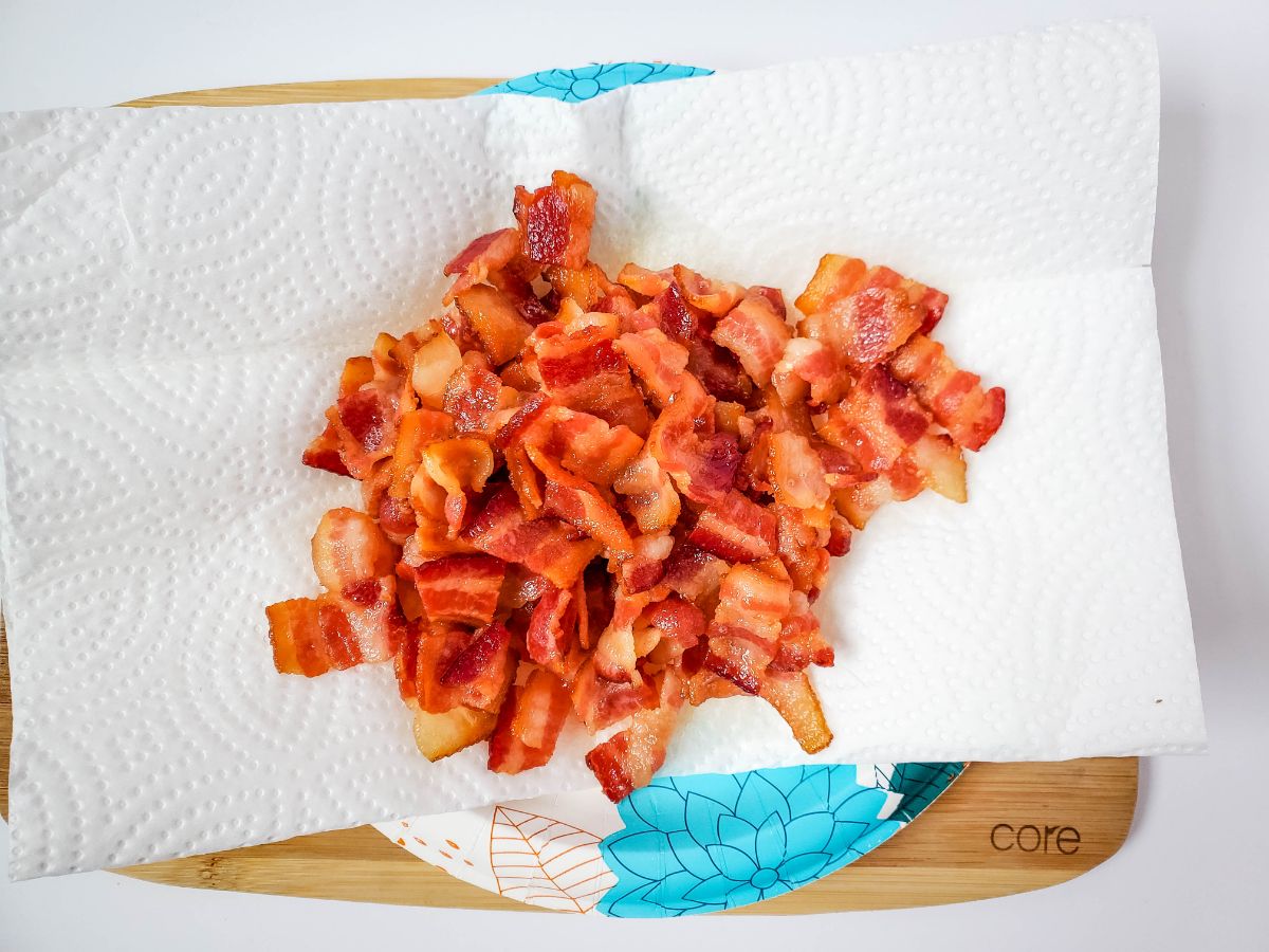Cooked bacon being drained using paper towels.
