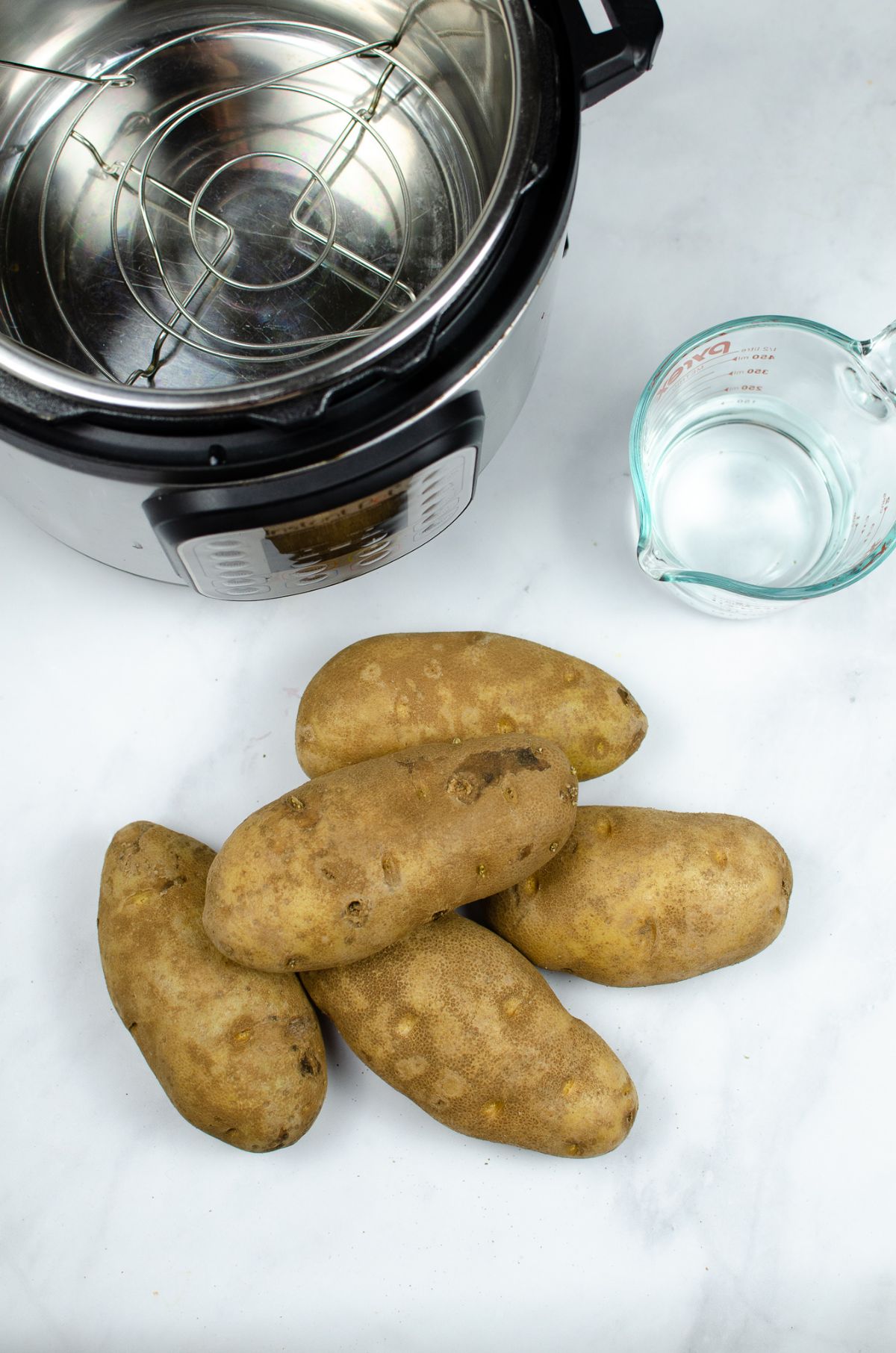Raw potatoes, water, and instant pot used to make Instant Pot Baked Potatoes.