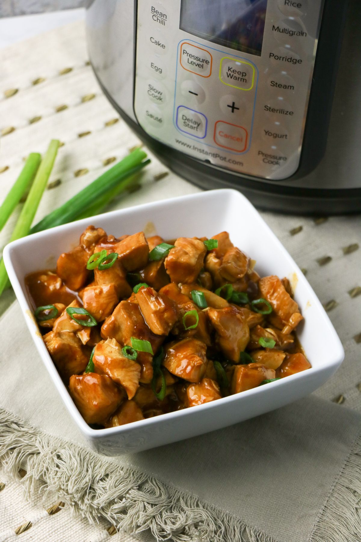 Instant Pot General Tso's Chicken in a white serving bowl next to an instant pot.
