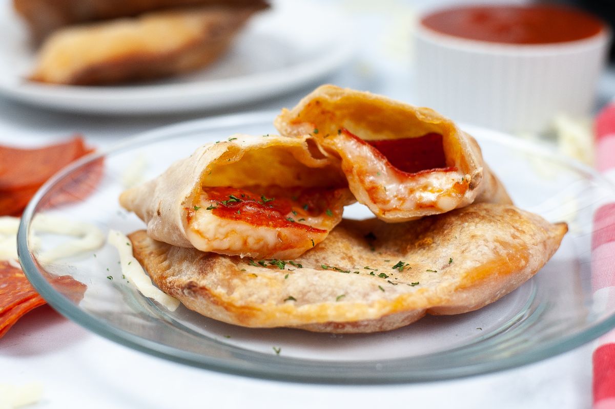 A horizontal image of a serving of 2 pieces of Air Fryer Calzone where one is halved on top of the other piece showcasing the melted cheese filling.