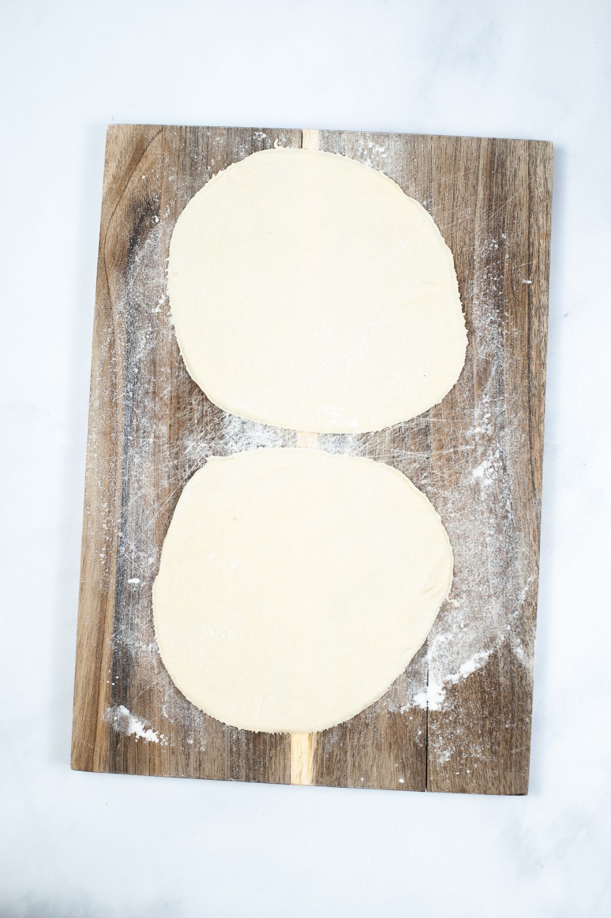 2 pieces of flattened dough, cut out into circles on a wooden board.