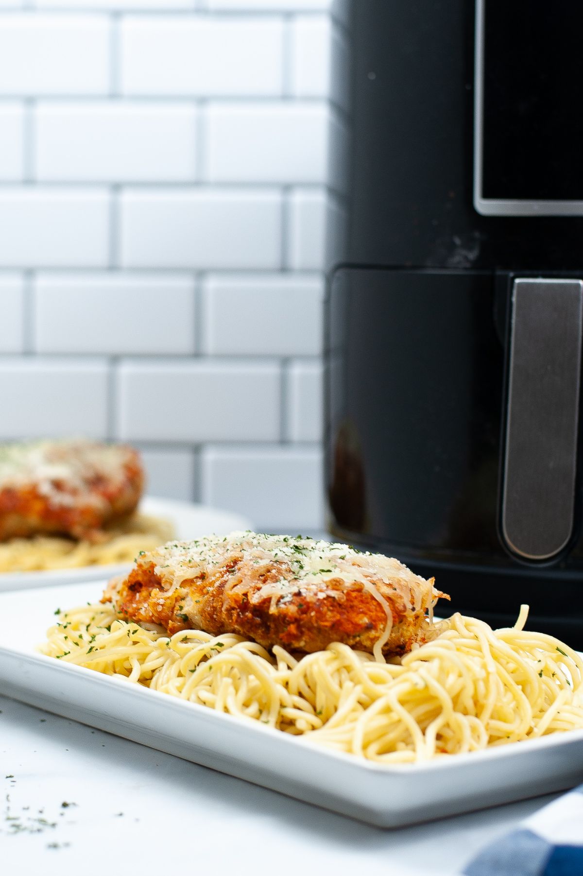 Air Fryer Chicken Parmesan on top of pasta on a white platter.