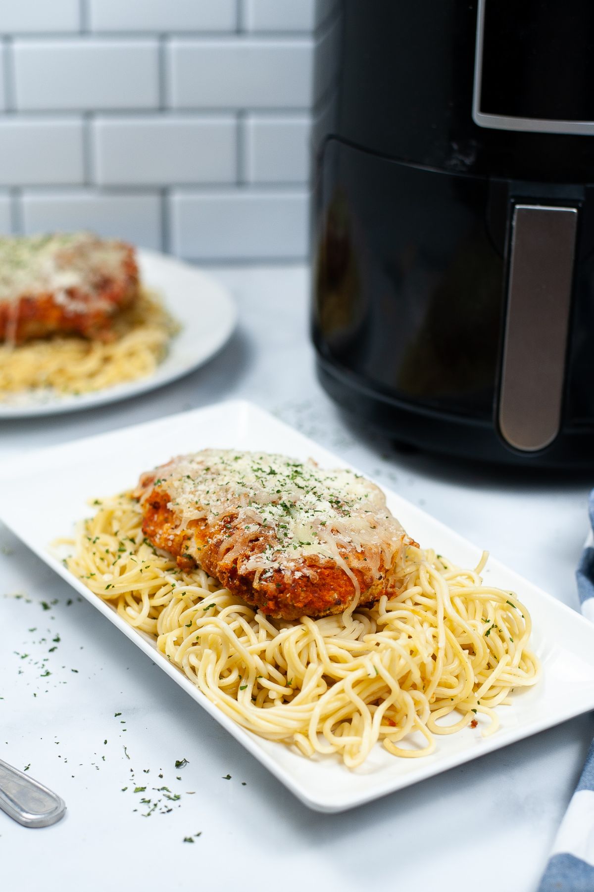 Air Fryer Chicken Parmesan on top of  pasta on a white platter.