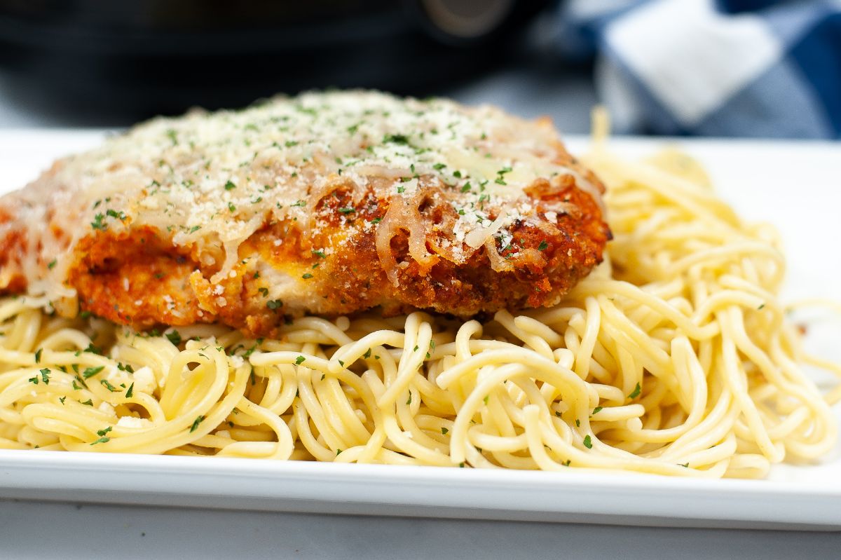 A close up horizontal shot of Air Fryer Chicken Parmesan on top of pasta on a white platter.