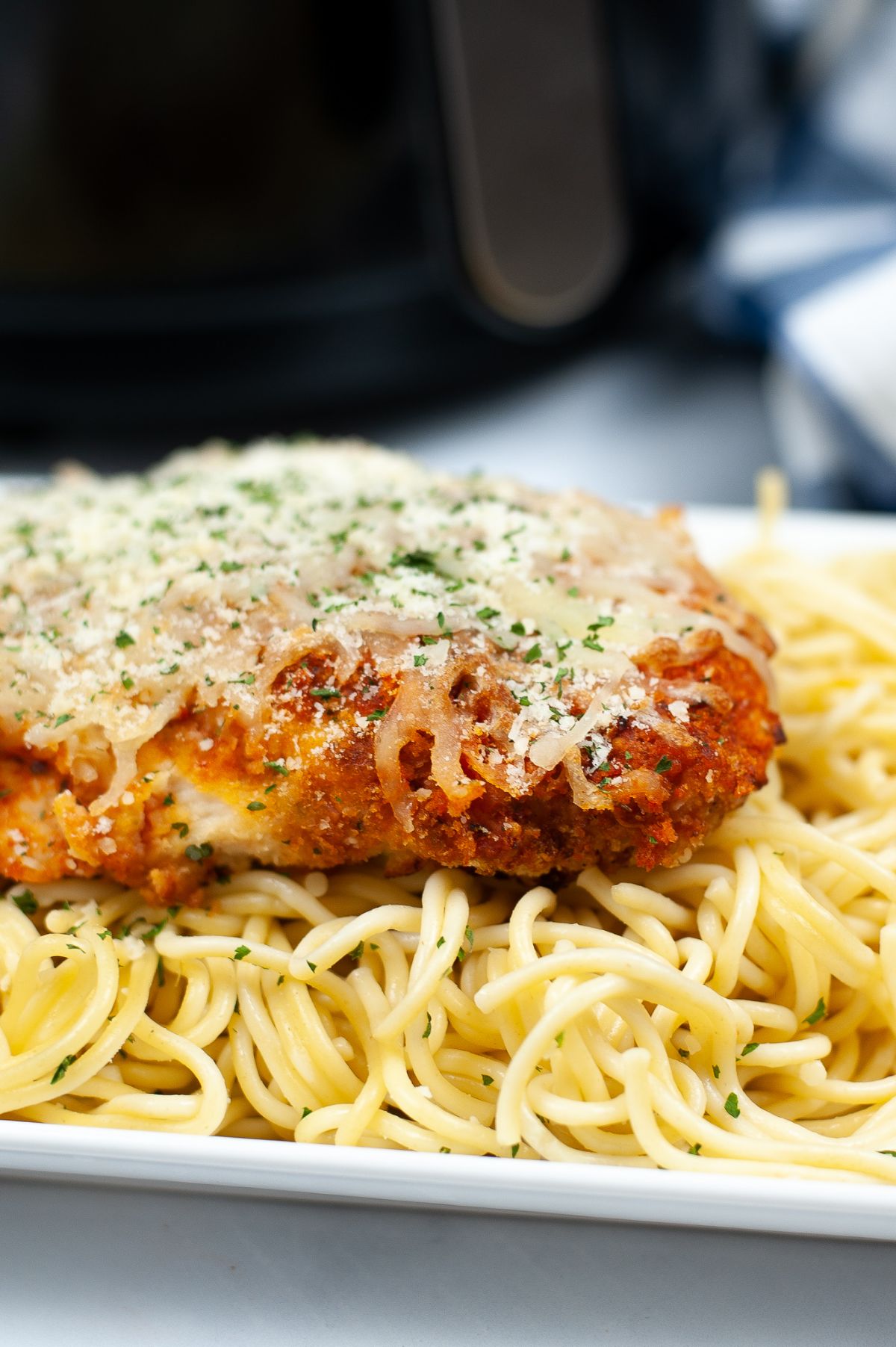 Close up shot of Air Fryer Chicken Parmesan on top of pasta on a white platter.