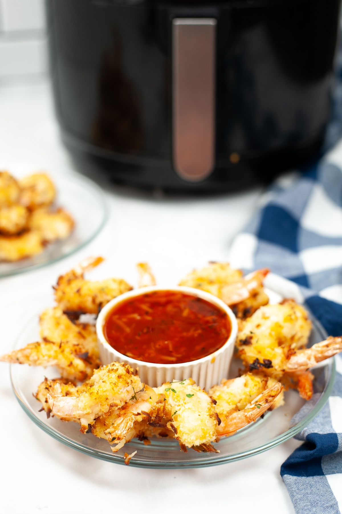 Pieces of Air Fryer Coconut Shrimp on a glass serving plate with a sauce in the middle.