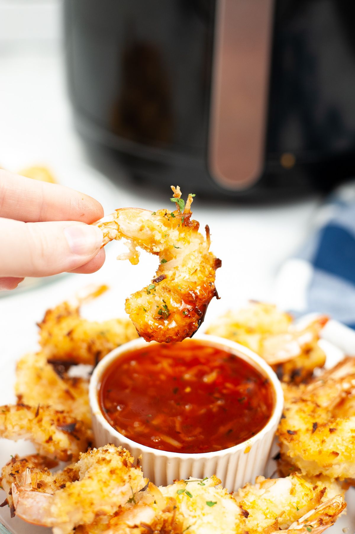 a hand holding an air fried Coconut Shrimp after dipping it in sauce.