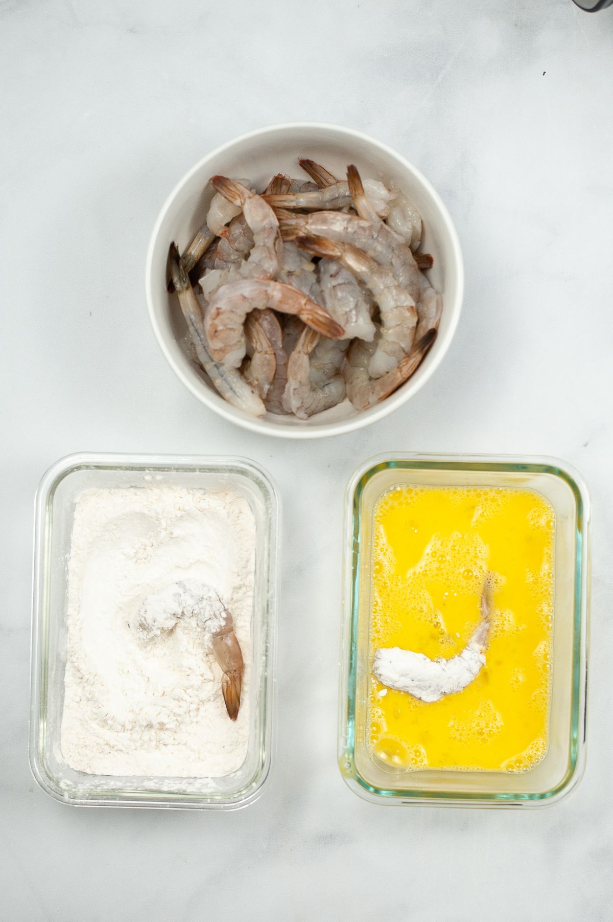 In three separate bowls are cleaned shrimp, flour and cornstarch mixture, whisked eggs.