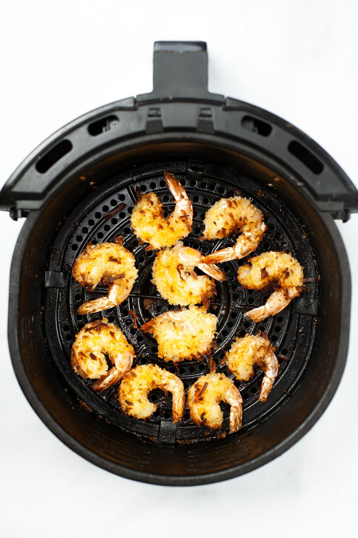 Cooked coconut shrimp in an air fryer basket.