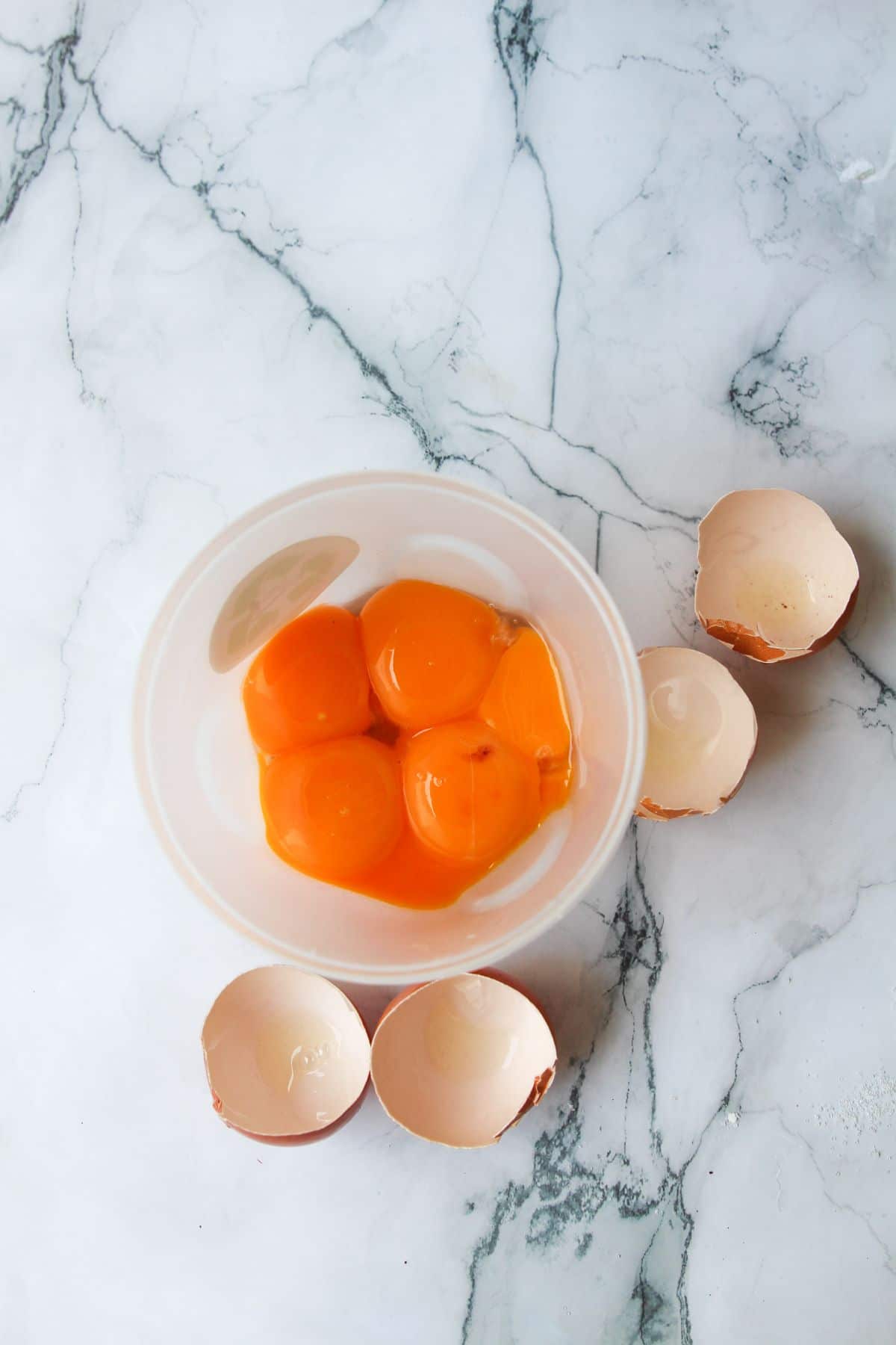 Egg yolks in a bowl next to cracked eggshells