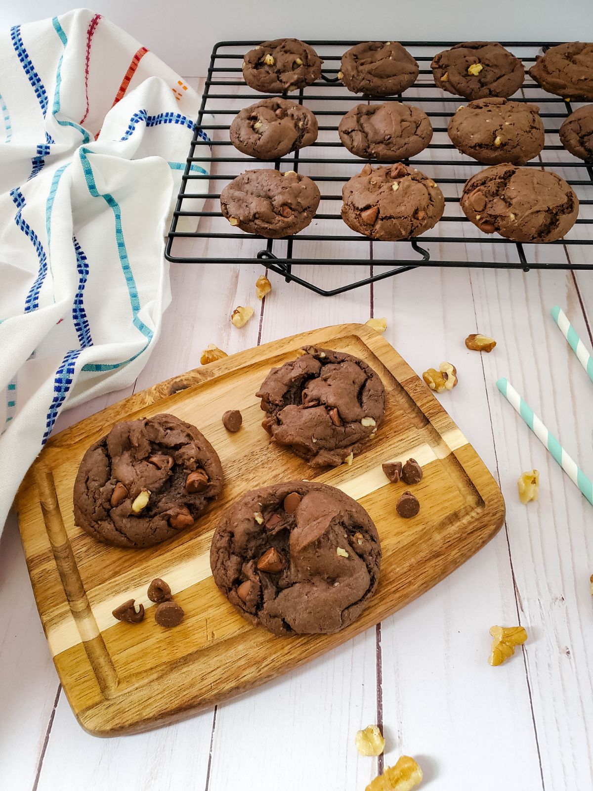 3 Double Chocolate Walnut Cake Mix Cookies on a wooden chopping board and the other cookies on a cooling rack.