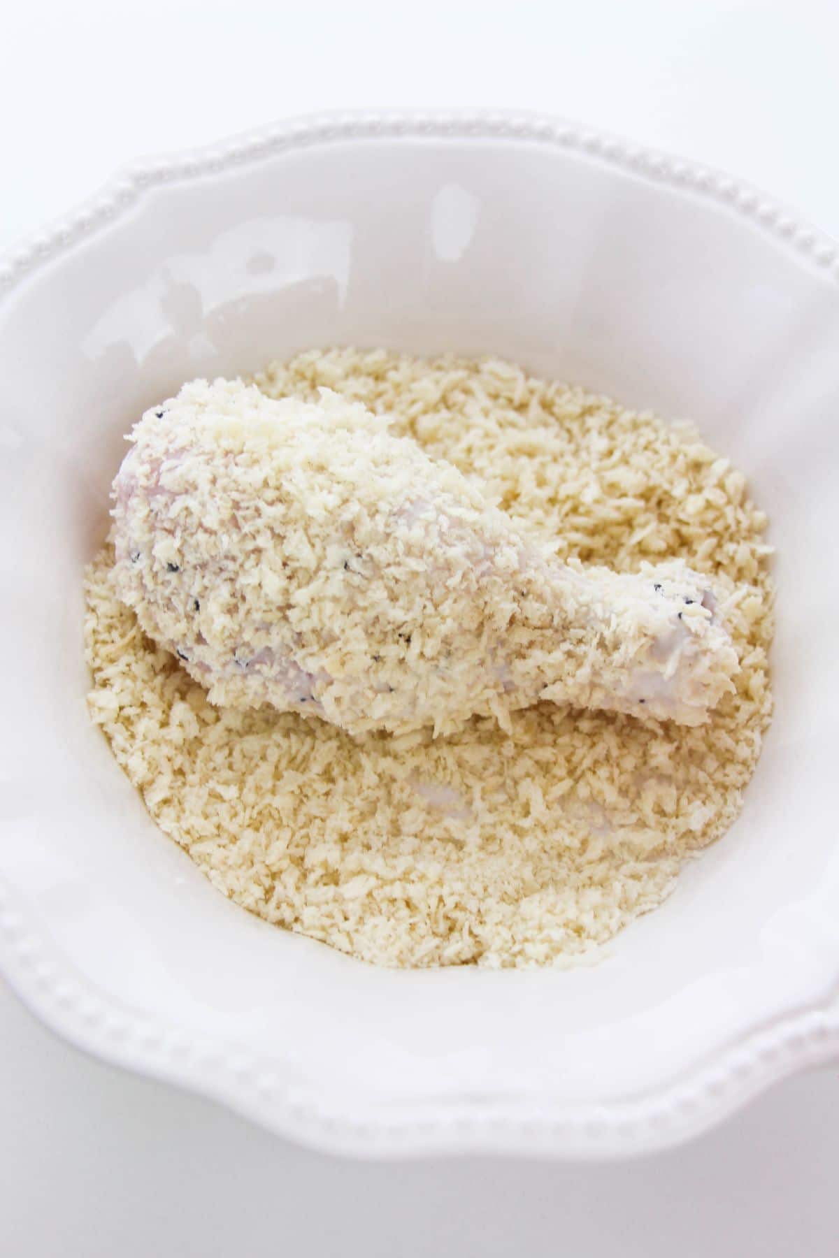 Chicken drumstick on the last bowl for dredging - breadcrumbs.