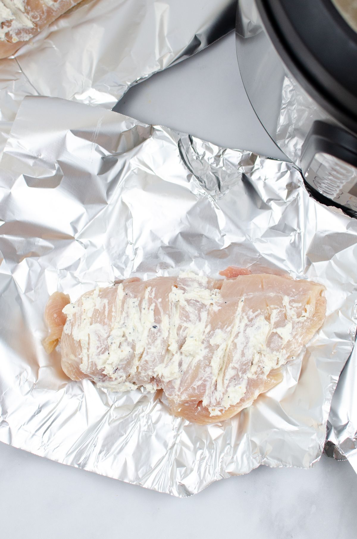 A piece of chicken breast on a foil topped with cream cheese.