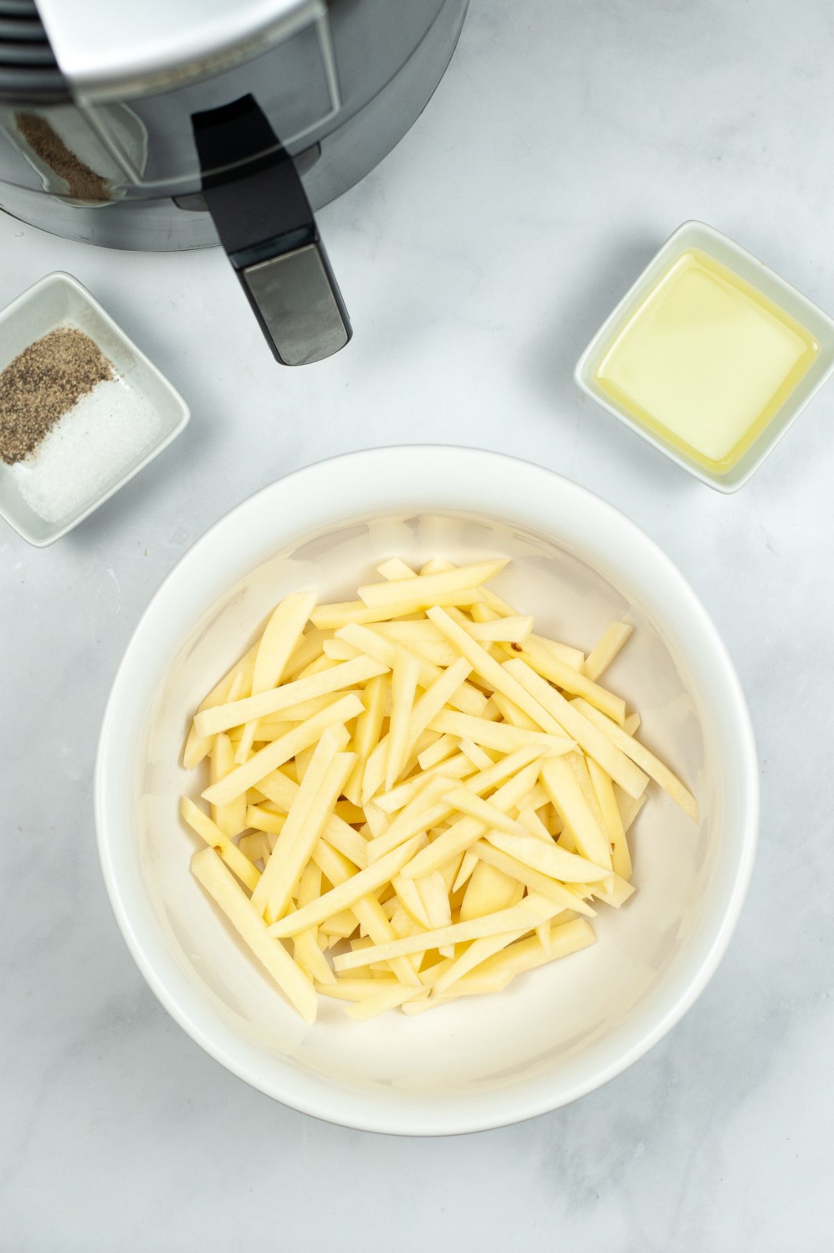 potatoes cut into long, fry-shaped lengths in a white bowl 