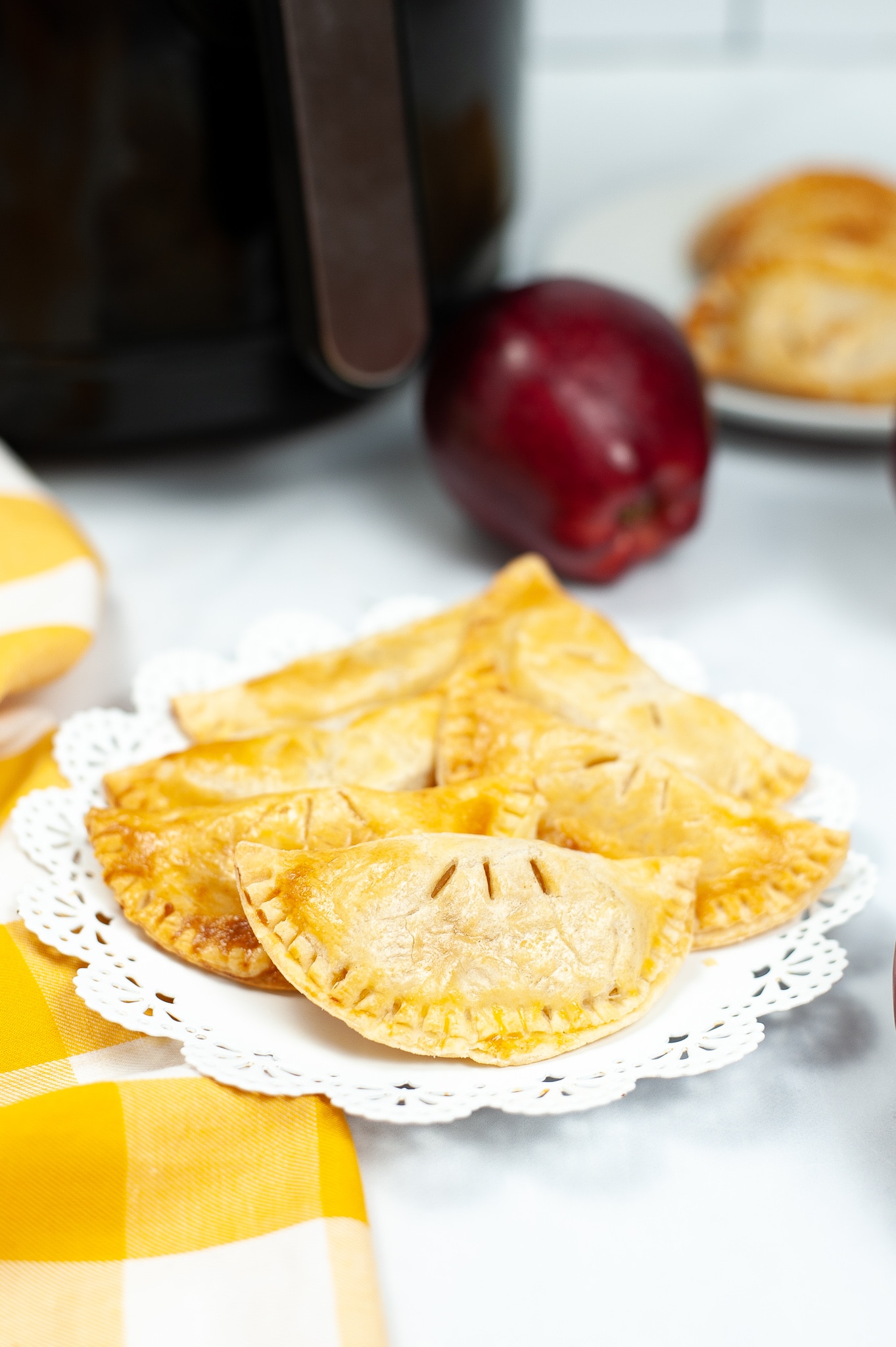 Caramel Apple Hand Pies on a white plate with an apple and an air fryer in the background