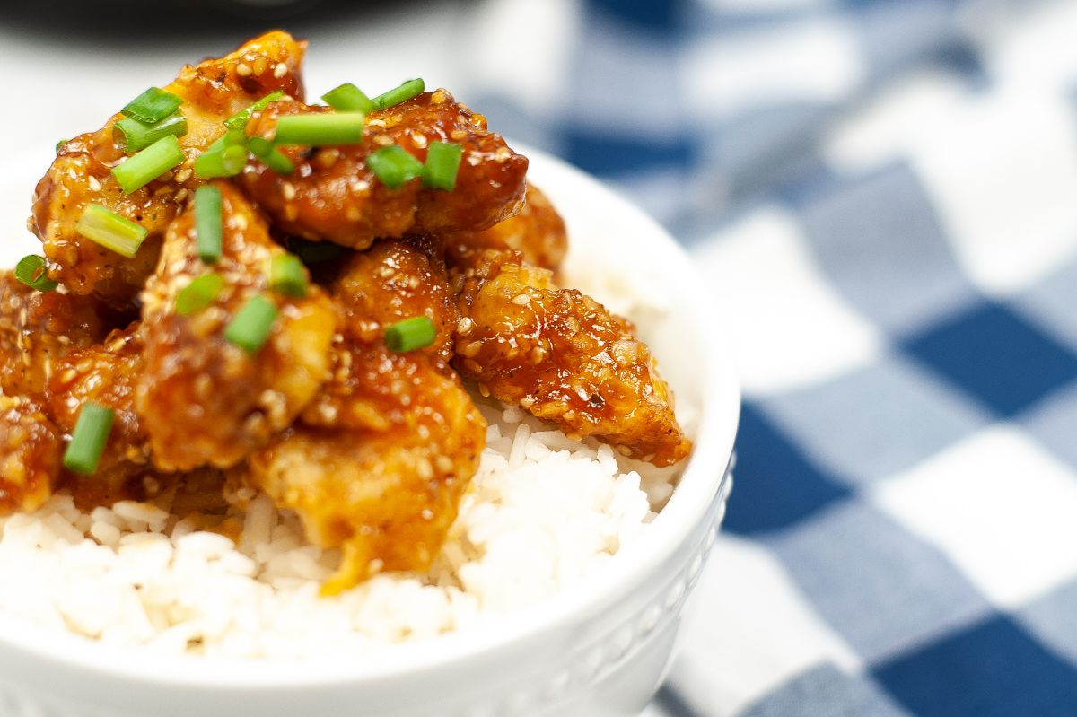 a closeup of Air Fryer Sesame Chicken in a white bowl topped with spring onion.