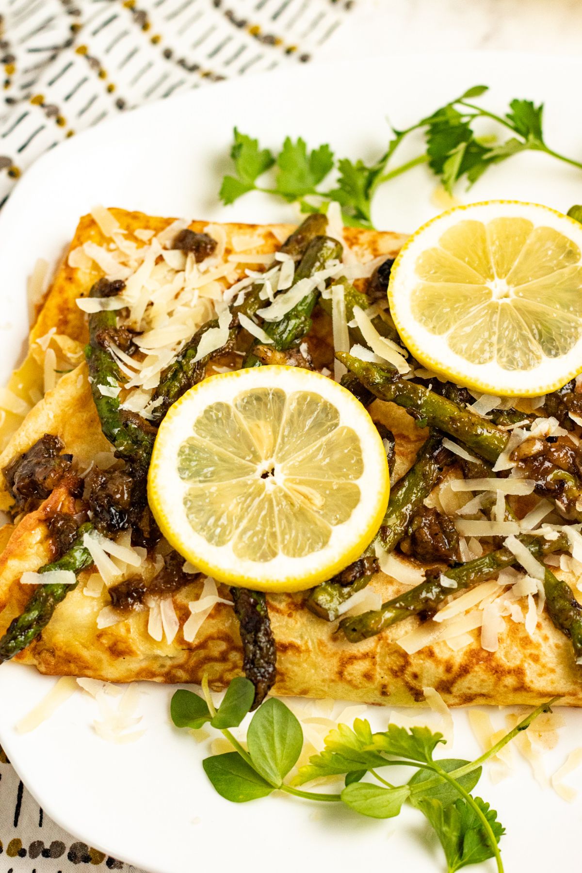 Chicken crepes on a white serving plate topped with asparagus, parmesan and lemon.