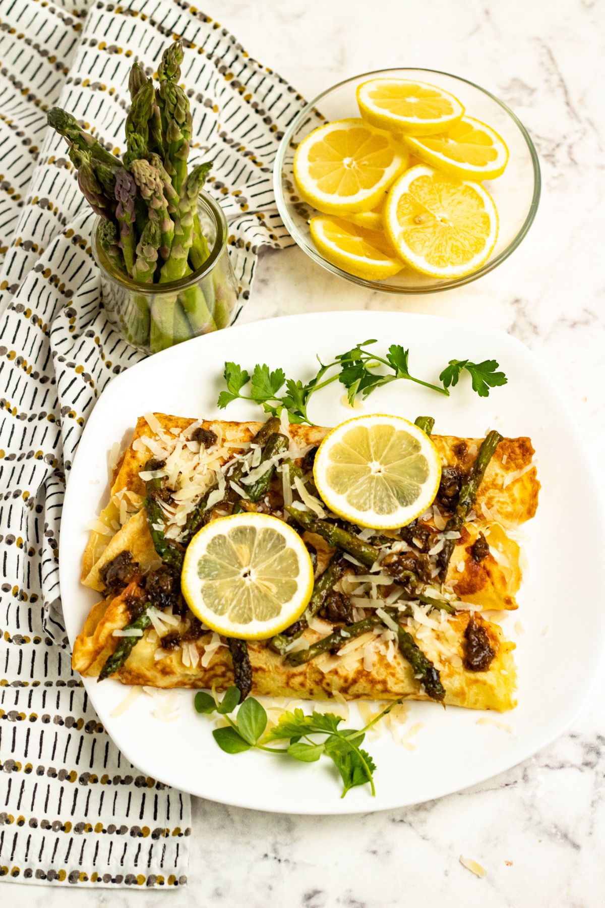 Chicken Asparagus Crepes on white serving plate topped with slices of lemon and parmesan.