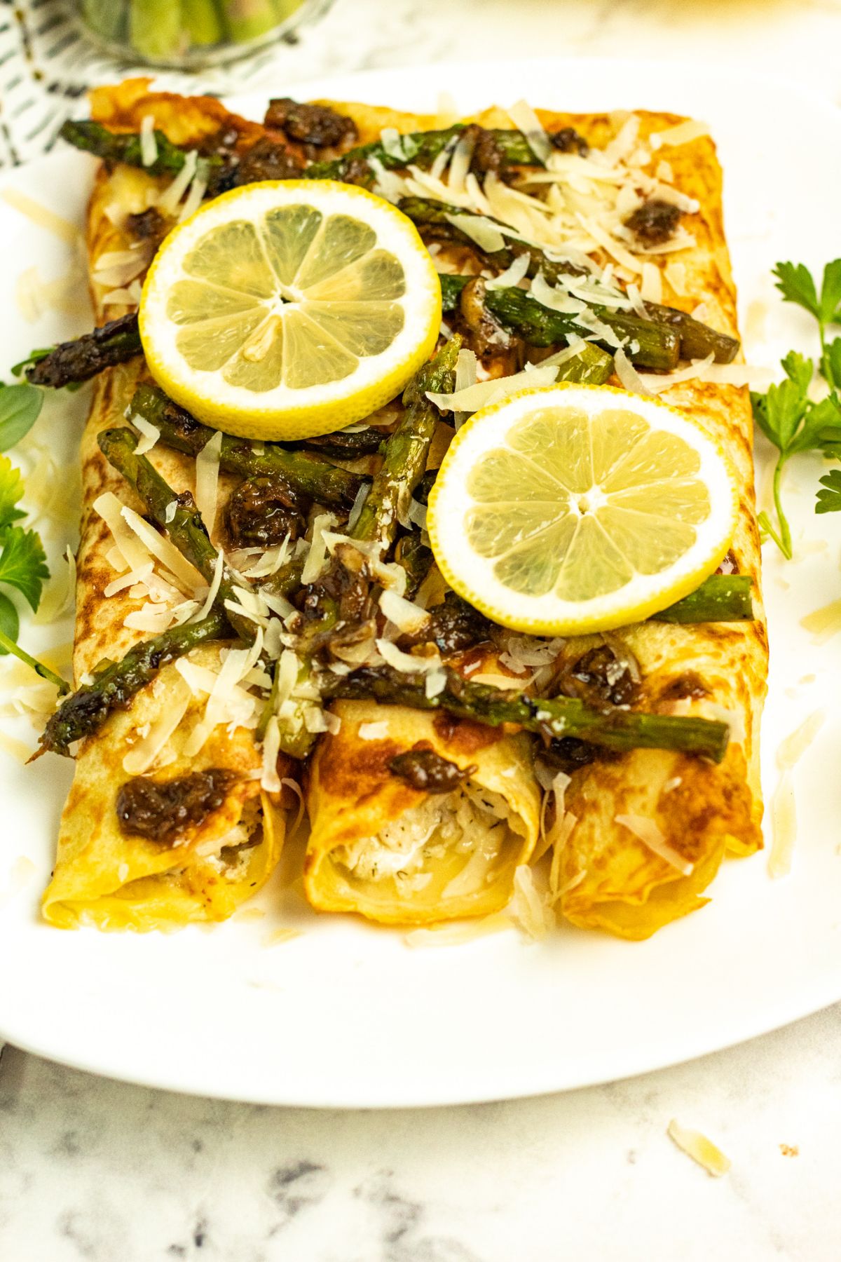 Chicken Asparagus Crepes on white serving plate topped with slices of lemon and parmesan.