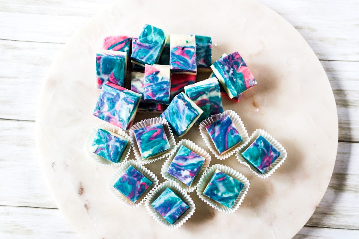 Cotton Candy Fudge cut into squares on a white plate, with some of them in muffin cup wrappers