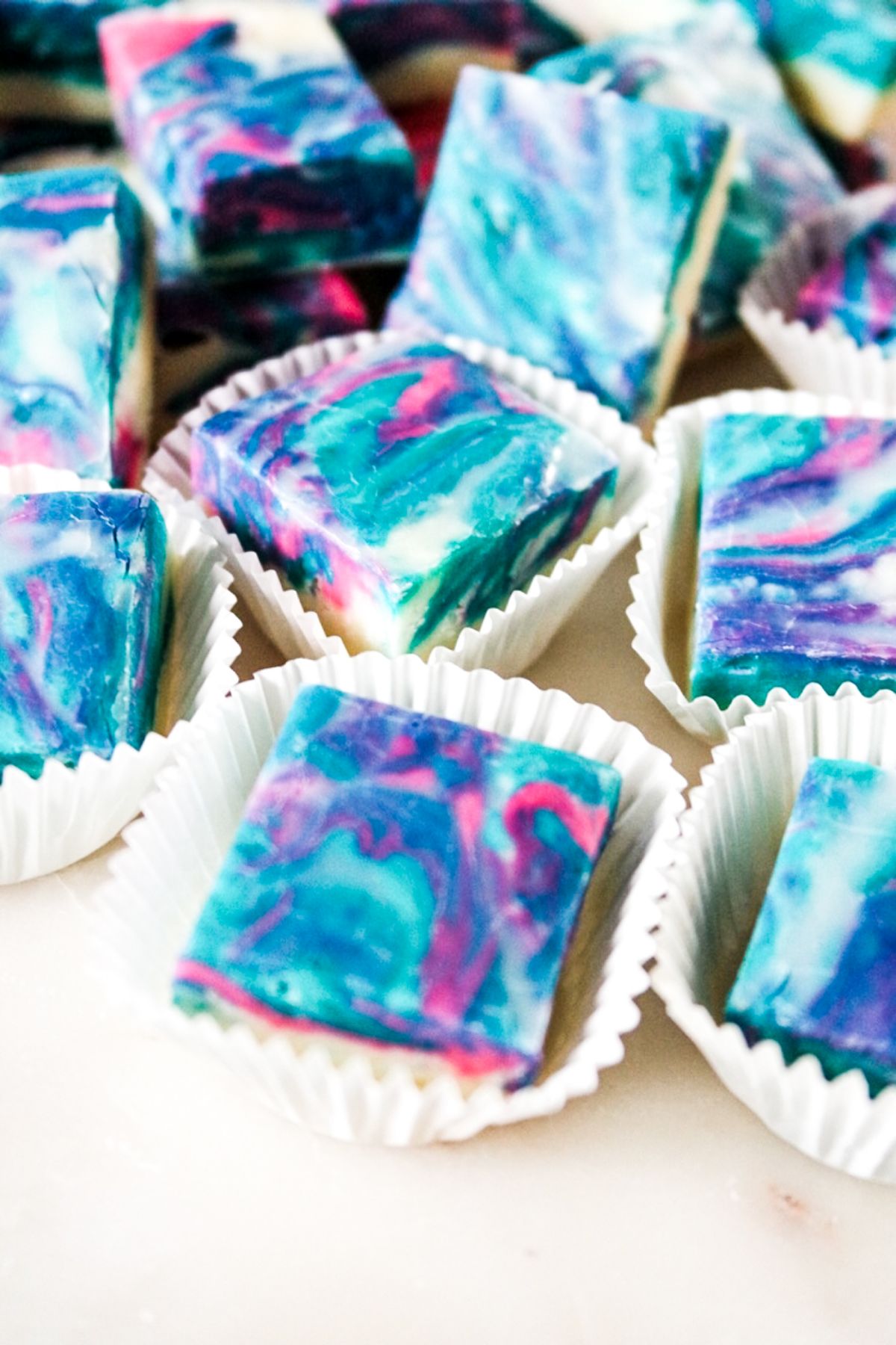 Close up shot of Cotton Candy Fudge in squares, with some of them in muffin cup wrappers.