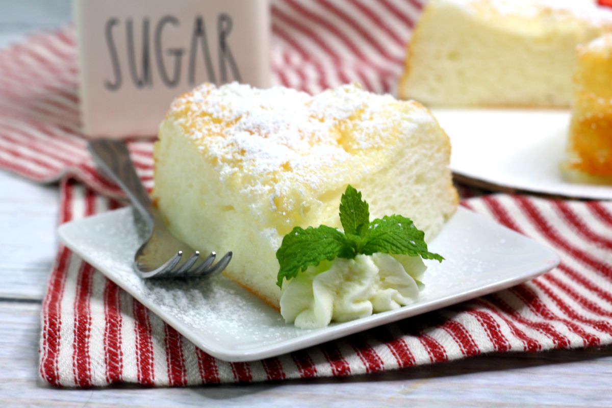 Instant Pot Angel Food Cake on white square plate topped with powder sugar and whipped cream on the side and topped with mint leaves. 