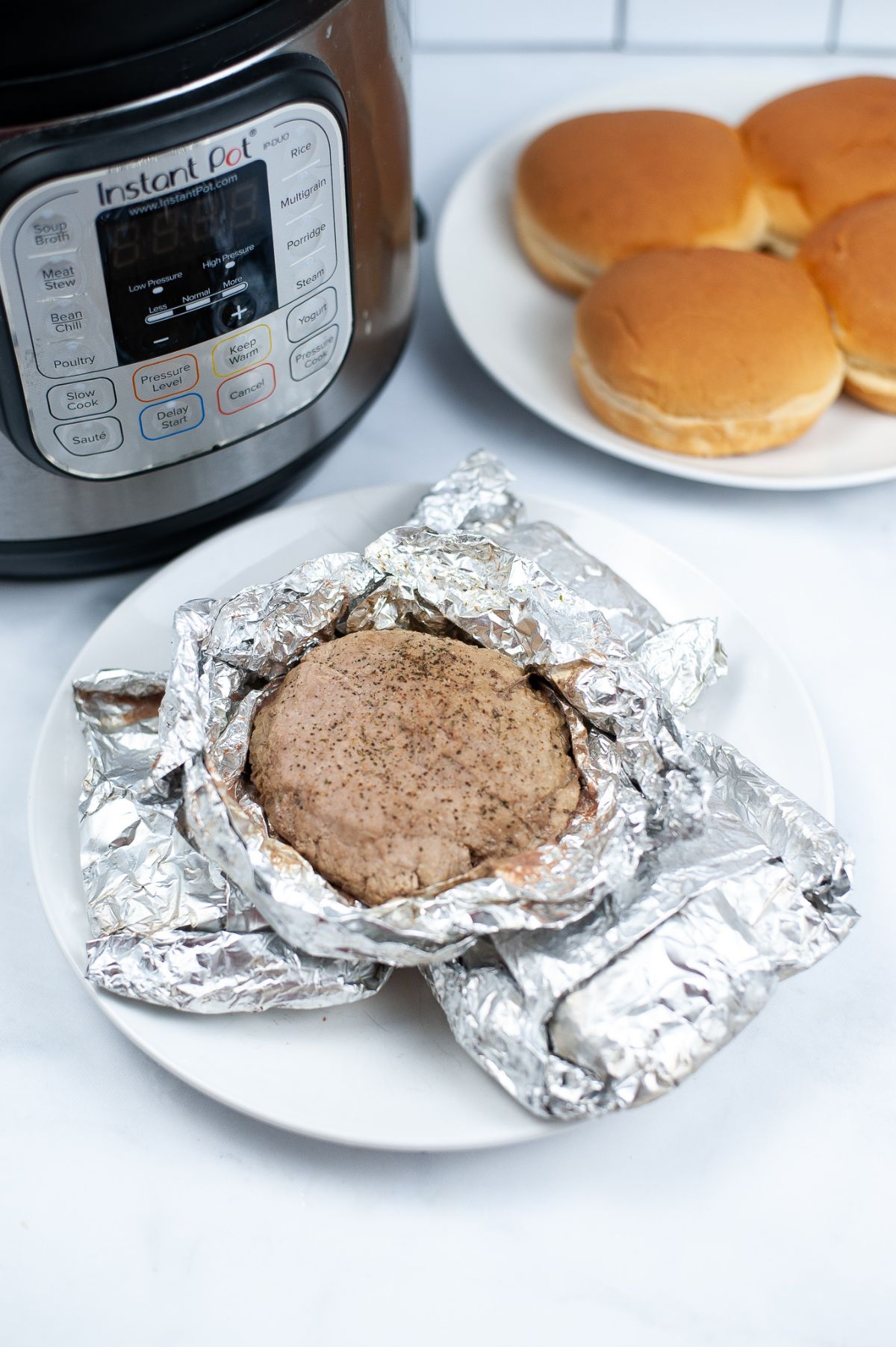 unwrapped cooked Turkey patties on a white plate with an instant pot and hamburger buns in the background. 