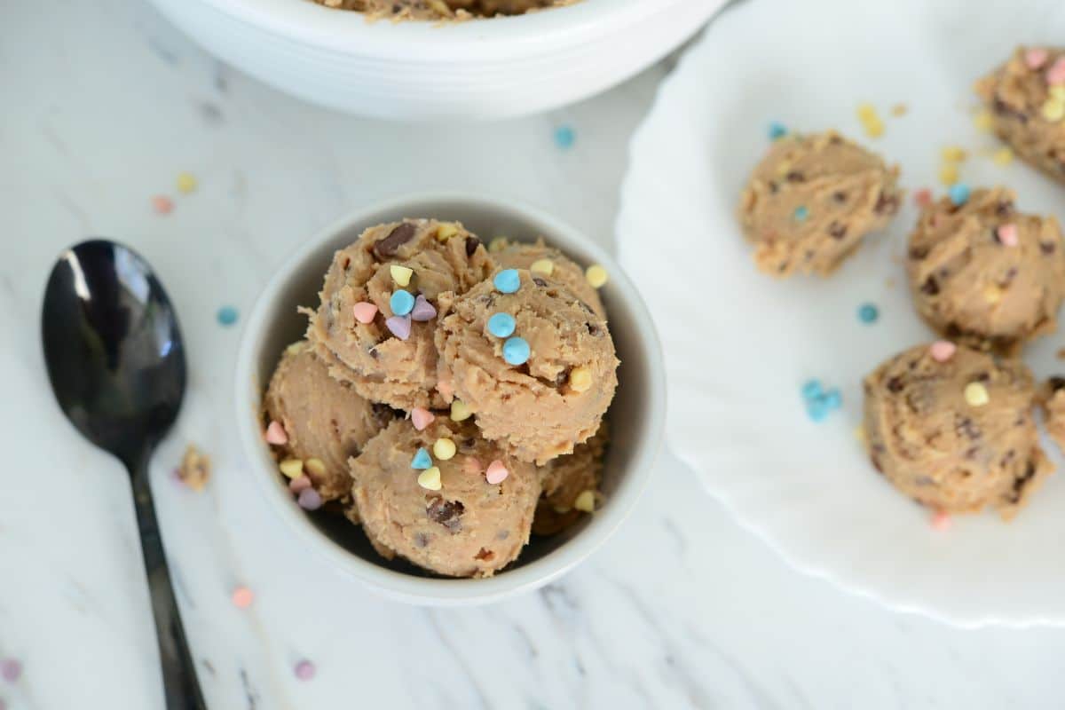 overhead shot of No Bake Cookie Dough Bites in a white bowl and on a white plate topped with pastel color sprinkles 