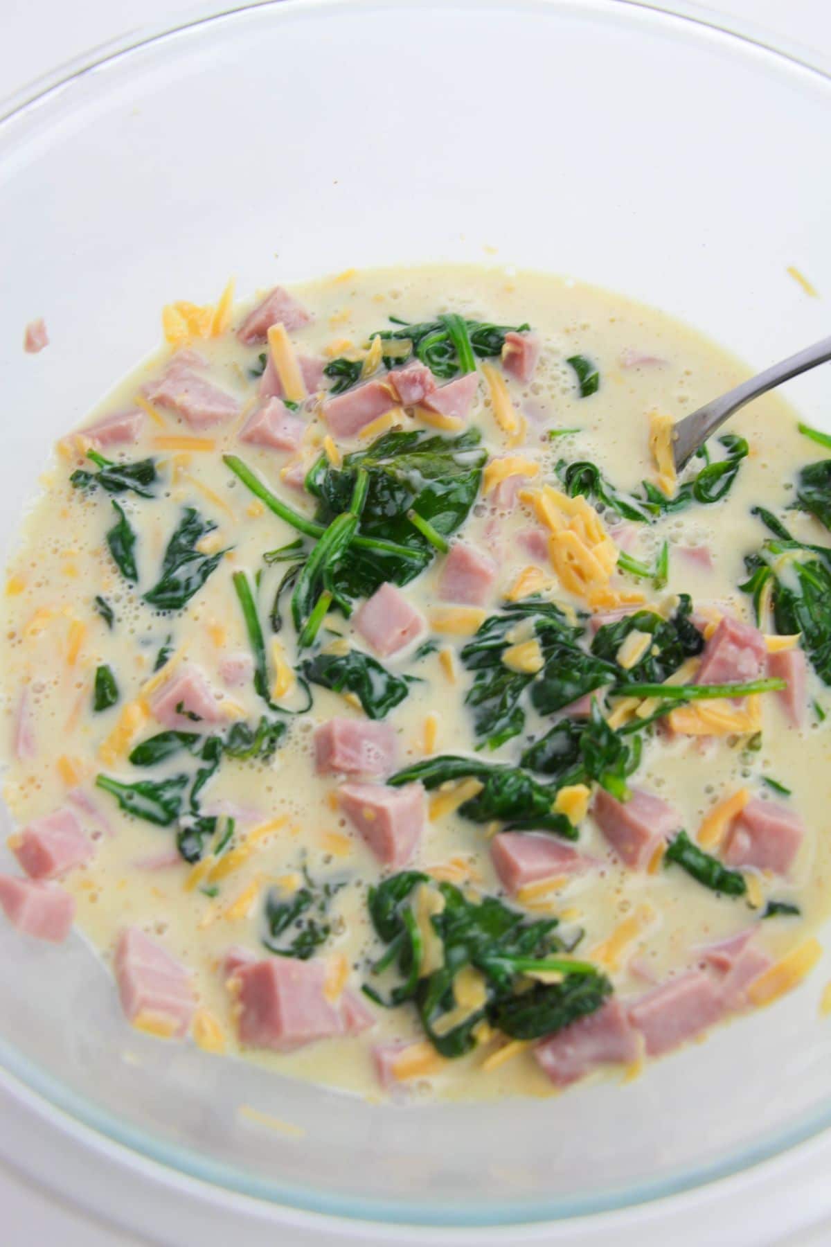 Mixture of ingredients for Ham Spinach Cheese Quiche in a transparent bowl
