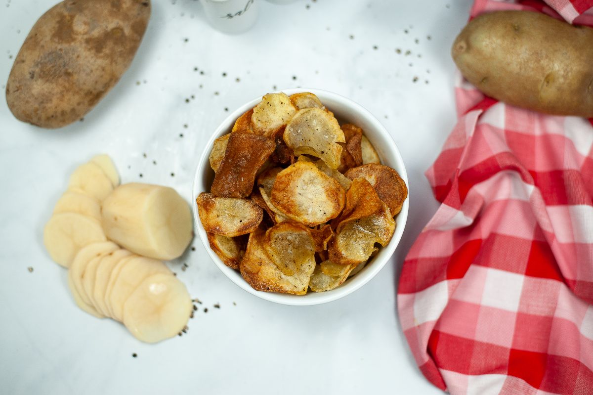 Homemade Air Fryer Potato Chips in white bowl  next to 2 potatoes and some slices of potatoes