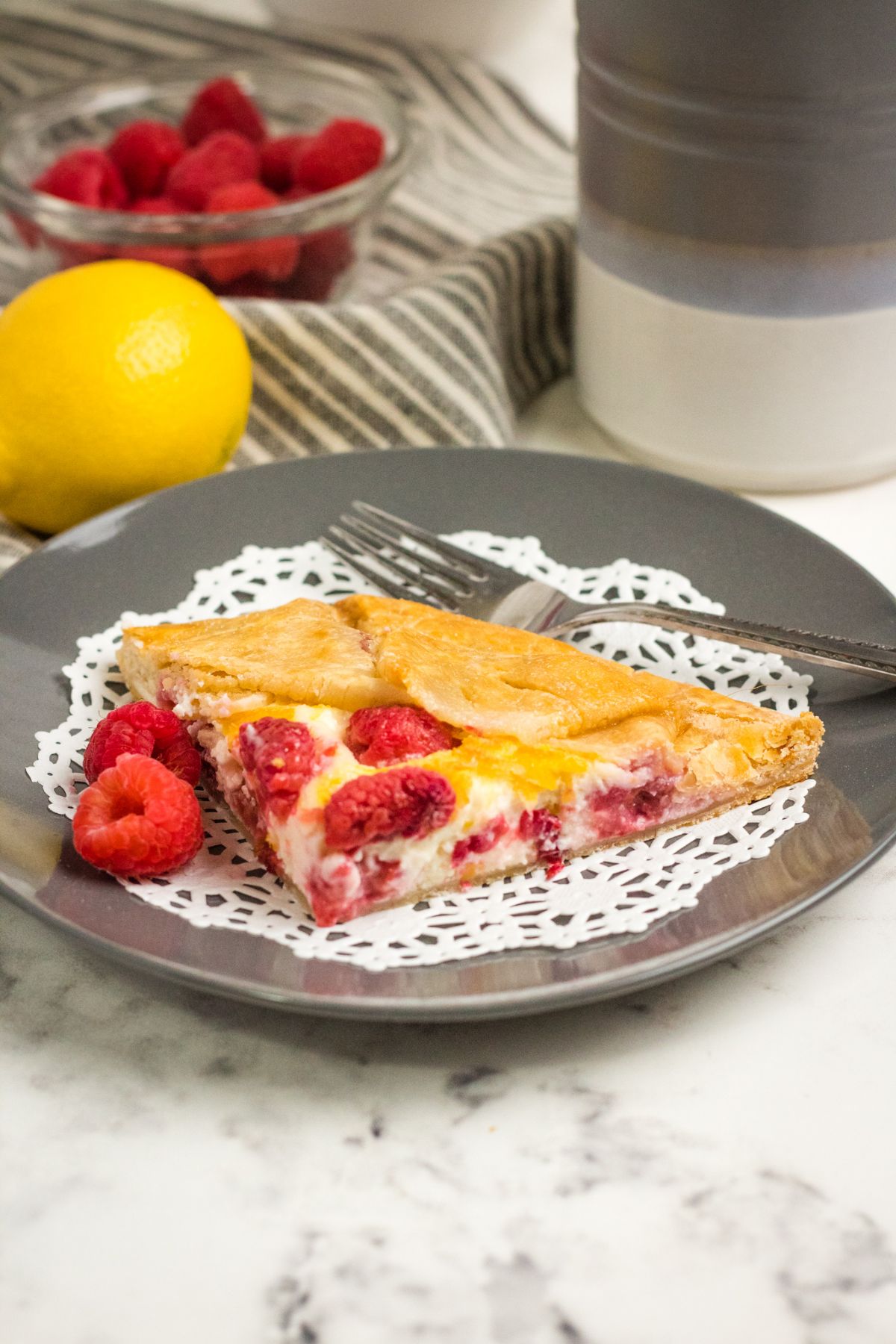 Raspberry Cream Cheese Galette on a gray plate. next to a lemon and a striped cloth