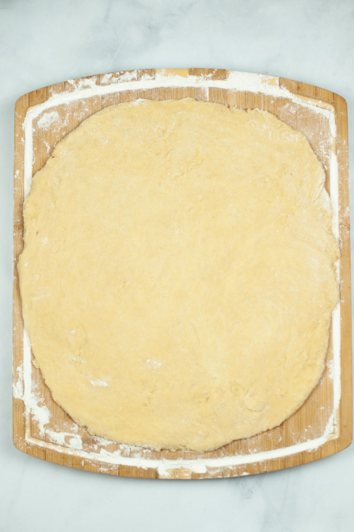 flattened dough on a wooden board dusted with flour