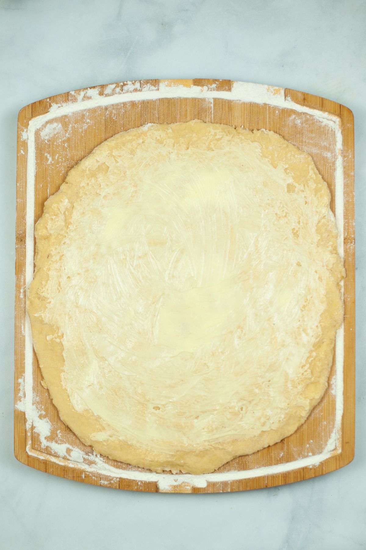 flattened dough spread with butter, on a wooden board