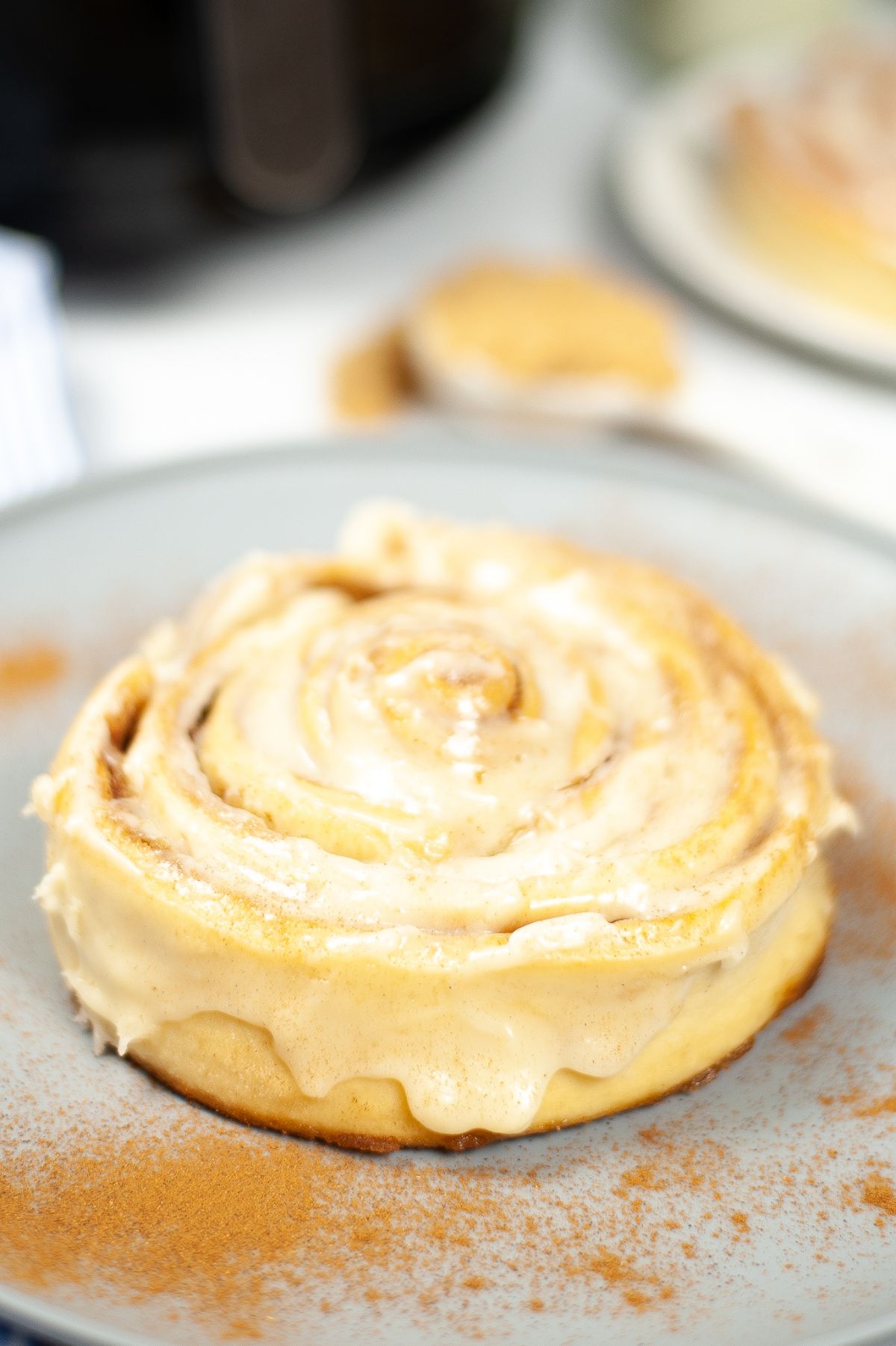 Air Fryer Copycat Cinnabon Cinnamon Roll topped with cream and dusted with cinnabon powder