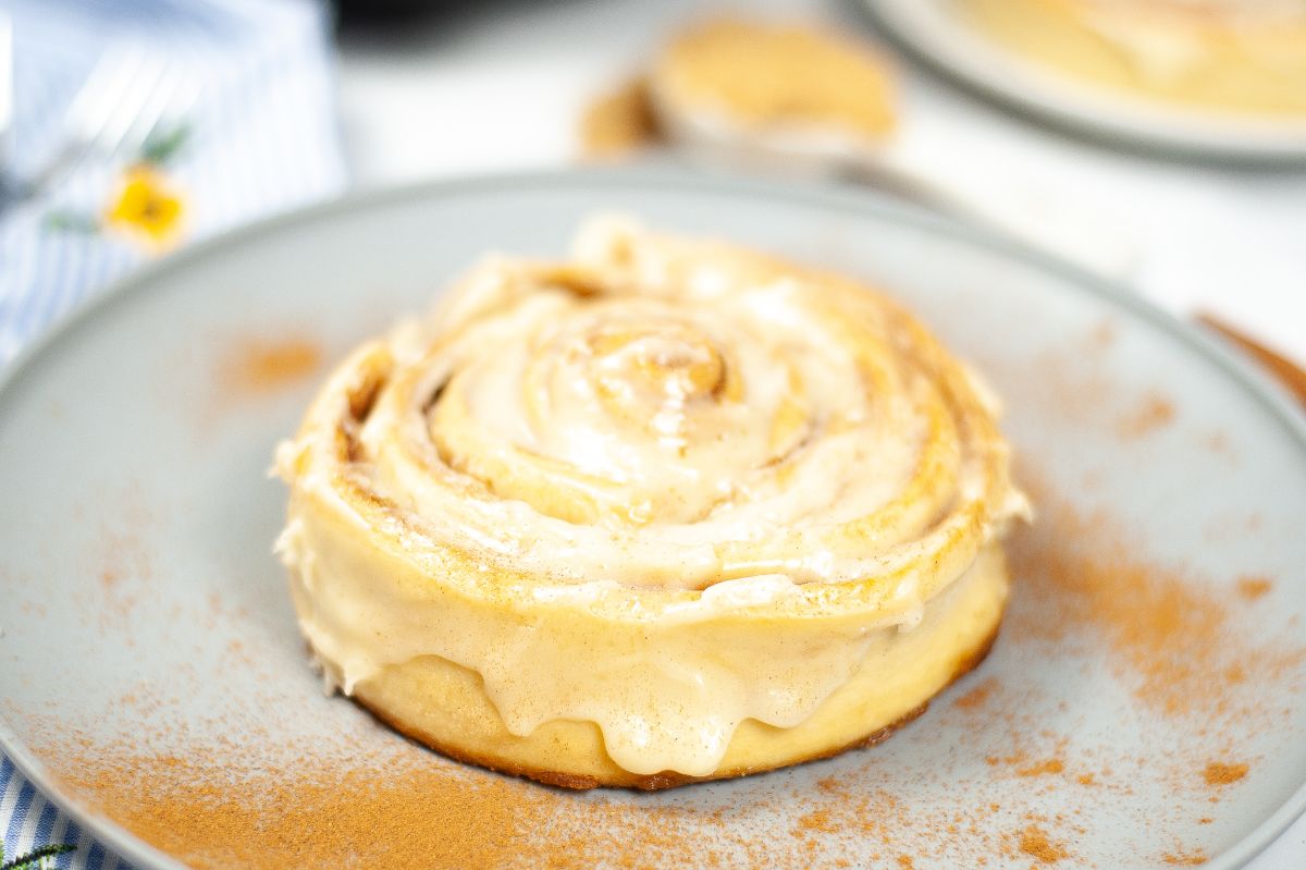 Air Fryer Copycat Cinnabon Cinnamon Roll topped with cream and dusted with cinnabon powder